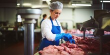 Woman Working In A Butchery, Wearing Protective Clothes And Gloves, Putting Minced Meat Into A Meat Grinder