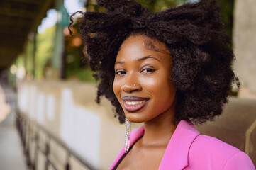 Fashion outdoor street style portrait of Beautiful young African American woman posing outside on urban city landscape summer day wearing pink jacket. Attractive black female, diversity concept