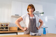 © Kawee - Caucasian senior elderly woman wearing apron, cleaning kitchen at home.