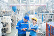 © Nutchapong Wuttisak - Half body photo of American male engineer and female manager Watching listnotes and meeting holding a radio Wear a helmet and uniform. in the plastic and steel industry There is a working machine