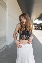 fashion cool hipster beautiful girl in a stylish lace top with a bra and a white skirt with a handba