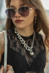 Wall Mural - Fashion female street portrait of beautiful stylish hipster woman with cool vintage sunglasses and jewelry in lace black fashion top with bra walks in the city