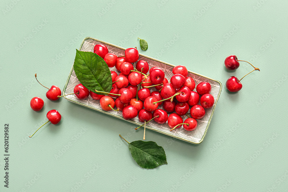 Plate with sweet cherries on green background