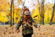Cute happy little girl in autumn park throwing leaves