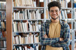 © AnnaStills - Portrait of adult student standing with his arms crossed and smiling at camera in library at college
