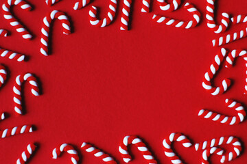 Flat lay Christmas composition with frame of candy canes on a red background. Copy space for text