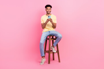 Full body photo of young satisfied man sitting chair use smartphone browsing safari internet web pages isolated on pink color background