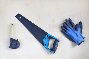 Sharp new hacksaw, sawing wood, hand tool and measuring tape and safety gloves on wooden surface