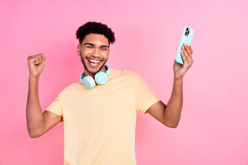 Poster - Portrait of satisfied optimistic man with afro hairstyle earrings stubble in headphones hold smartphone isolated on pink color background