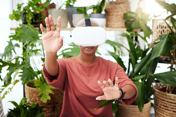 Poster - Woman, virtual reality and headset with hands at home for metaverse, 3d world or future. Black person with plants and vr glasses for ecology, ai and touch for interaction, video game or experience
