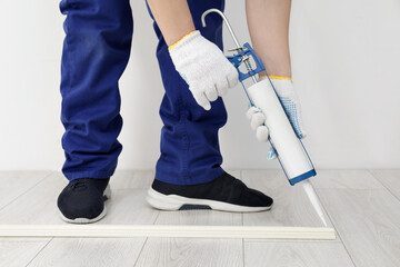 Sticker - Man using caulking gun while installing plinth on laminated floor in room, closeup