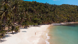 Fototapeta  - Piękna rajska plaża z białym piaskiem, palmami i turkusową wodą, osoba idąca po wybrzeżu.