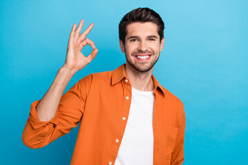 Fototapete - Photo of cheerful positive man dressed orange shirt smiling showing okey gesture isolated blue color background