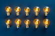 © ink drop - Overhead flat lay view of a collection of glowing yellow light bulbs on a blue background