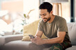 canvas print picture - Happy, man and texting on cellphone in living room for online mobile app, scroll social media and notification on sofa. Asian male person typing on smartphone, contact and internet download at home