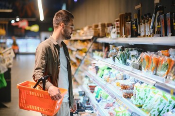 Handsome man buying some healthy food and drink in modern supermarket or grocery store. Lifestyle and consumerism concept