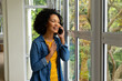 Happy biracial woman talking on smartphone and looking out window at home