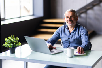 Mature man using laptop on desk at home and drink coffee