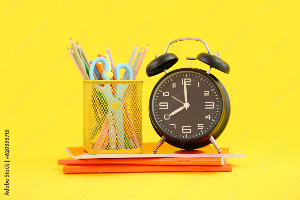 Alarm clock with notebooks and  stationery holder on yellow background
