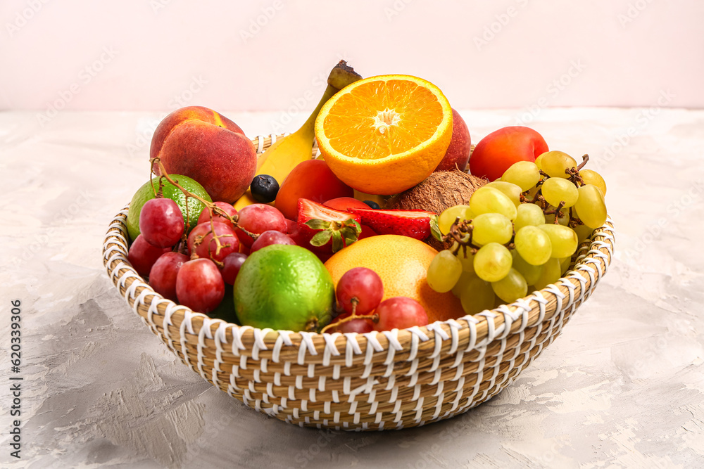 Wicker bowl with different fresh fruits on white table