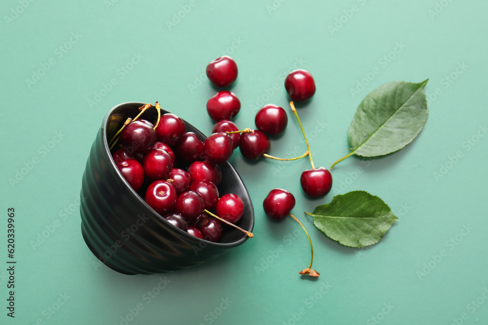 Bowl with sweet cherries on green background