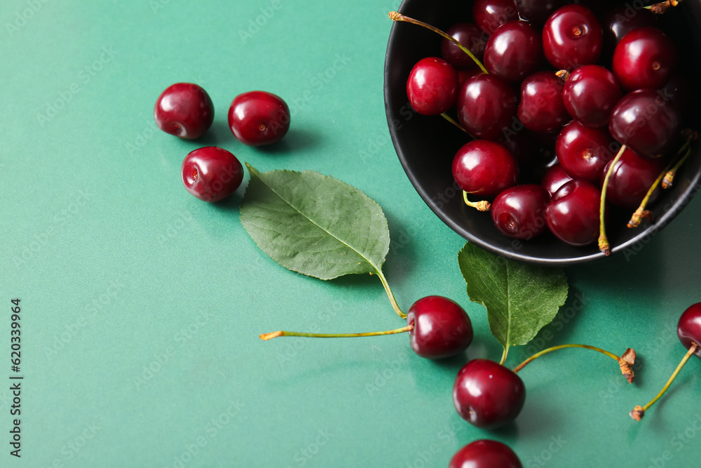 Bowl with sweet cherries on green background