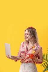 Wall Mural - Young woman with laptop and summer cocktail on yellow background