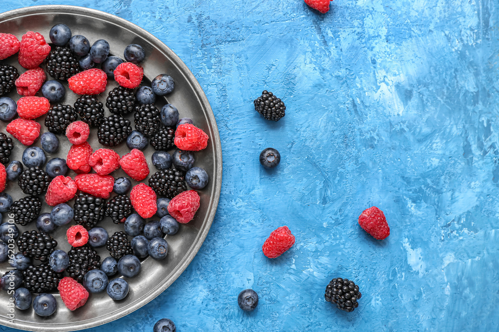 Plate with different fresh berries on blue background