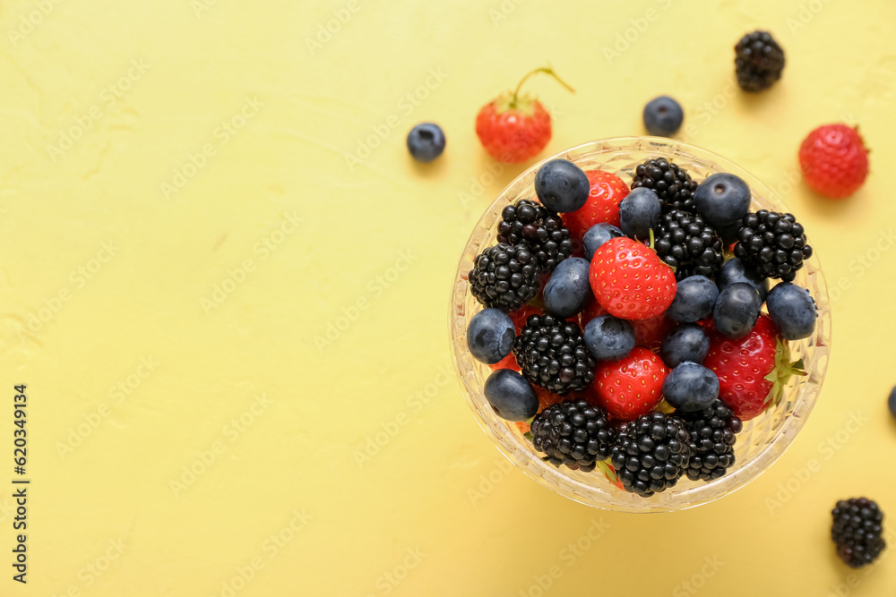 Bowl with fresh berries on yellow background, closeup