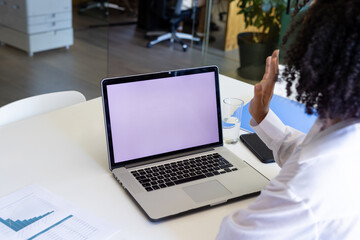Biracial casual businesswoman using laptop with copy space making video call and waving in office
