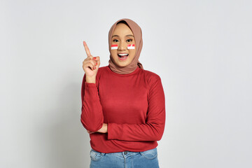 Excited young Asian woman having creative idea, pointing finger up at copy space isolated on white background. Indonesian independence day concept