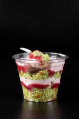 Wall Mural - Takeway cake in a glass with pistachios, strawberry mousse and strawberry confit on black background