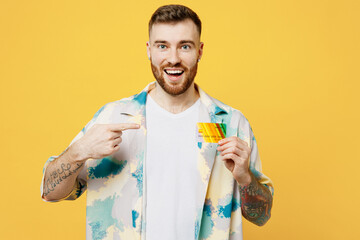 Young surprised happy man he wear blue shirt white t-shirt casual clothes hold in hand point finger on mock up of credit bank card isolated on plain yellow background. Tattoo translates life is fight.