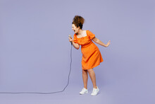 Full Body Side View Young Expressive Latin Woman Wear Orange Blouse Casual Clothes Sing Song In Microphone At Karaoke Club Isolated On Plain Pastel Light Purple Background Studio. Lifestyle Concept