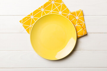 Wall Mural - Top view on colored background empty round yellow plate on tablecloth for food. Empty dish on napkin with space for your design