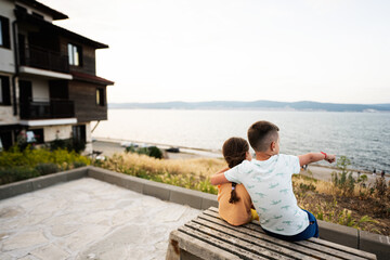 Back view of boy and girl sitting on bench and looking at sea in Nessebar.