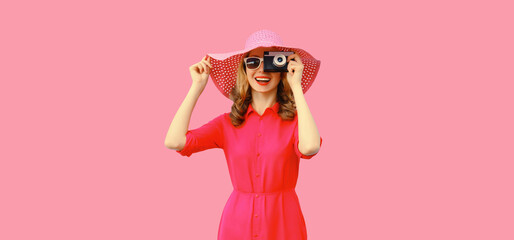 Wall Mural - Summer portrait of happy smiling young woman photographer with film camera wearing straw hat, pink dress, sunglasses on background