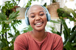 © Lategan/peopleimages.com - Relax, music and portrait of black woman with plants in home for wellness, happiness and calm. Nature, headphones and face of female person listening to audio with ferns, leaves and house plant