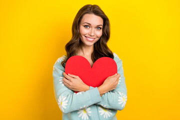 Wall Mural - Photo of sweet adorable woman wear turquoise cardigan smiling embracing red heart isolated yellow color background