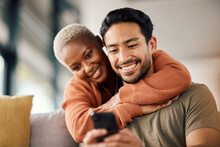 Phone, Interracial Couple And Technology On A Sofa At Home Reading Text In A Living Room. Support, Young People And Hug Together In A House Sitting On A Lounge Couch With Mobile Streaming And Video