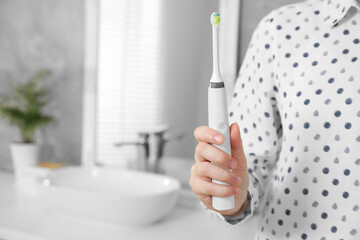 Woman holding electric toothbrush in bathroom at home, closeup. Space for text