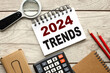 2024 trends. 2024 trends on apricot crush background, wooden background open notepad with text near calculator