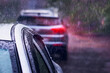 Leinwandbild Motiv Heavy rain falls on the roof of a car during a thunderstorm. Red brake light in the dark. The concept of auto insurance and natural disasters. Driving on cloudy rainy days. Selective focus.