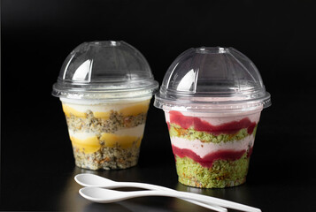 Wall Mural - Take away cakes in glasses with pistachios, strawberry mousse, poppy seed biscuit, and lemon curd on black background