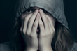 Close-up portrait of a fearful young girl with a hood covering her eyes and face with her hands - mental health, isolated, black background