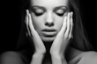 Close-up black and white portrait of a beautiful young woman with eyes closed covering / cupping her face with her hands - skin care, isolated, black background