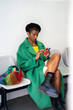 © Alba Vitta/Stocksy - African queer man using smartphone in waiting room