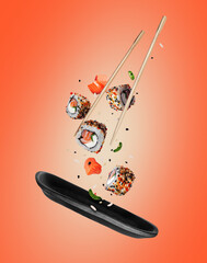 Wall Mural - Fresh sushi rolls with various ingredients falling on a black clay plate on a red background