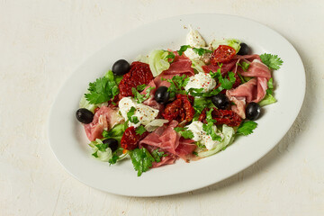 salad with dried tomatoes, prosciutto, soft cheese, olives, homemade, top view,