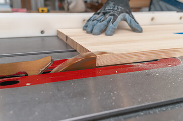 Wall Mural - Close-up view of cutting a wooden board with a circular saw. Carpenter's hand in a glove.